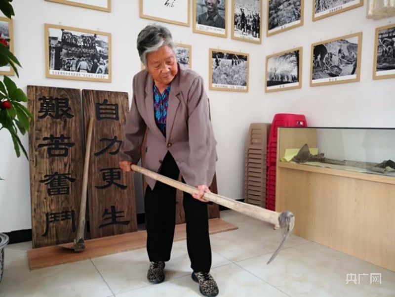 在"红色家风馆"里,侯秀珍手拿"传家宝"镢头(记者 雷恺 摄)