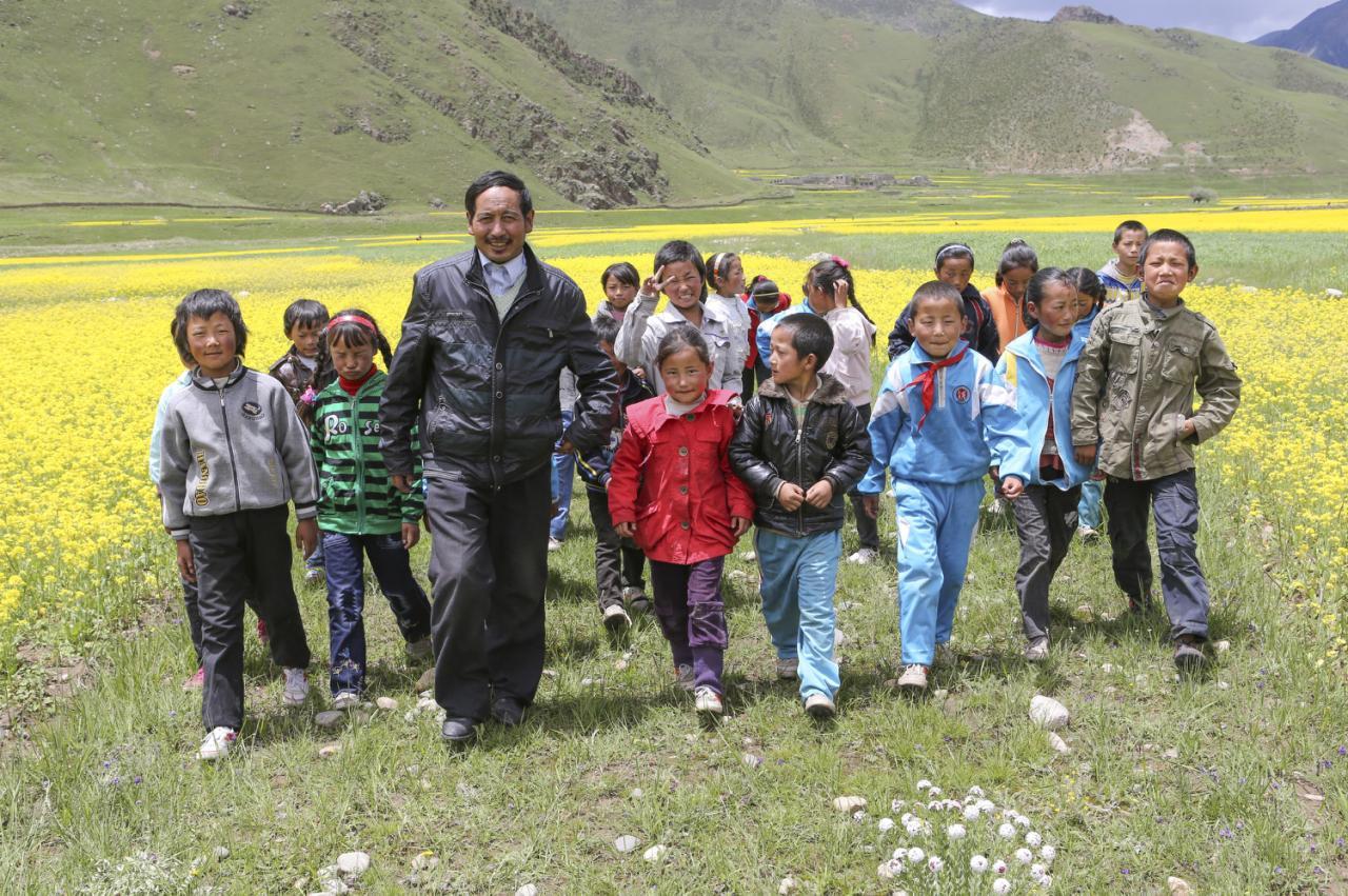 【图说:林周县拉岗完小次仁罗布校长带领学生走在油菜地里】"用乡村