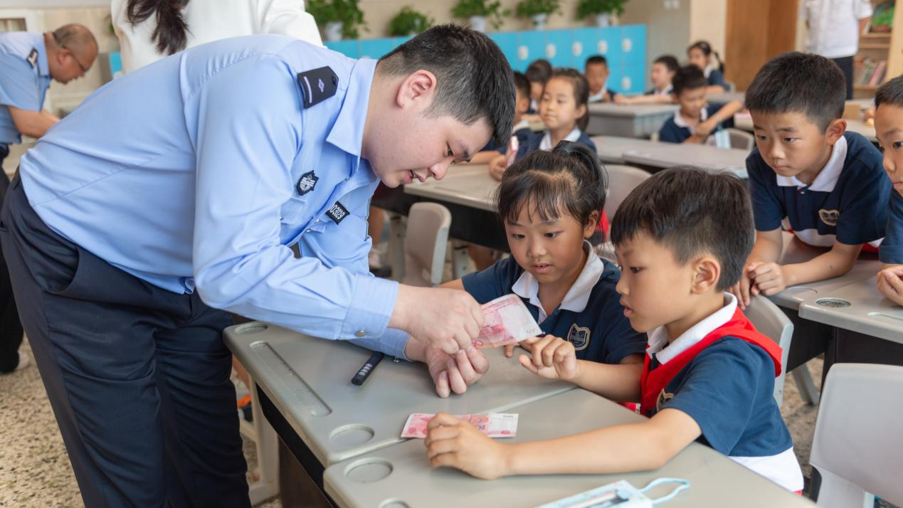 民警教一年级的学生识别人民币真伪(两江新区公安分局供图)在小学一
